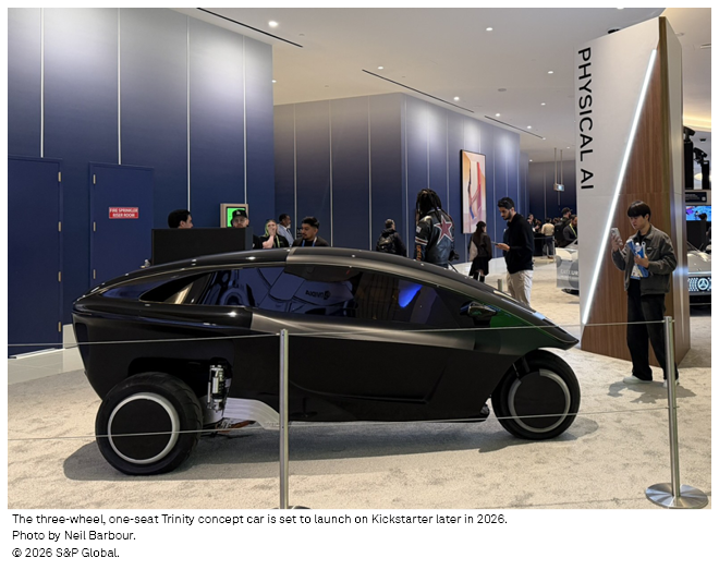 A sleek, three-wheeled Trinity concept car is displayed at an event, showcasing its futuristic design and technology.